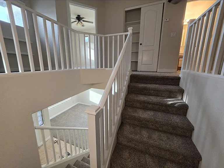 Carpeted upstairs landing with open railing, linen shelving, and easy access to nearby bedrooms and bath.