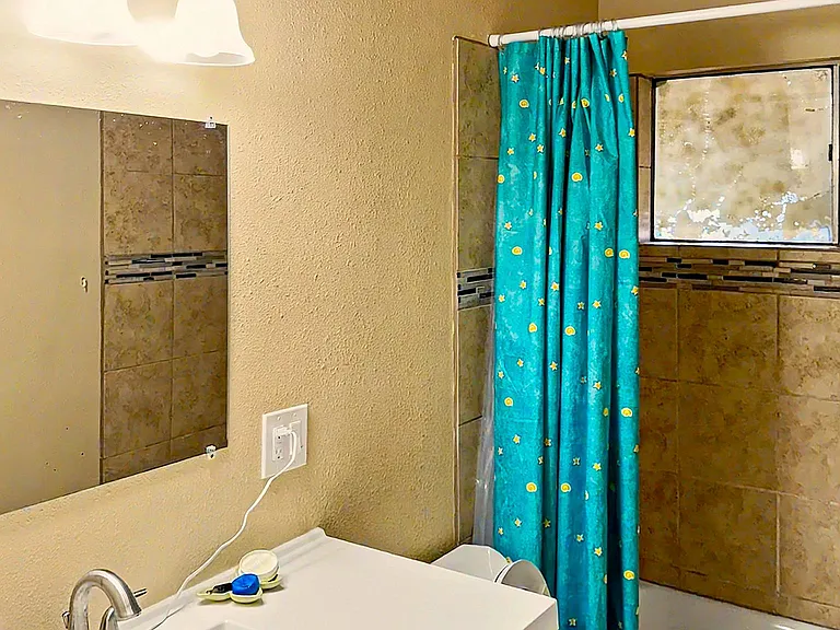 Full bathroom with vanity storage, wall mirror, and a shower/tub combo with tiled surround and window for ventilation.