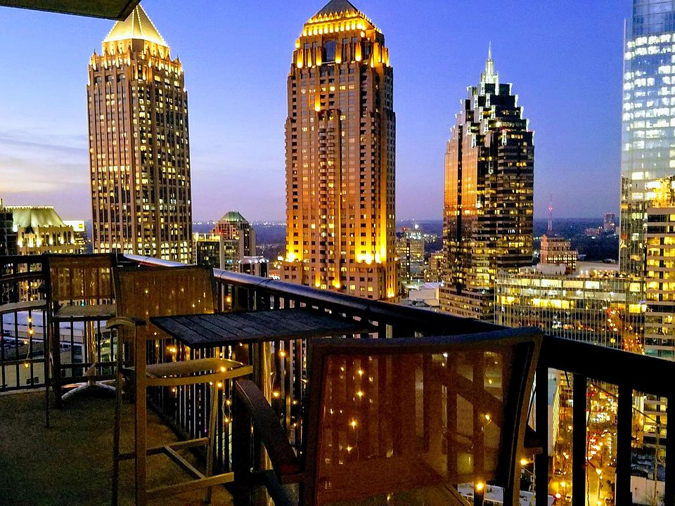 Private wrap-around balcony as seen in the evening, walking out from the living room. Balcony comes furnished with 3 hightop tables, 6 hightop chairs, and an IR heat lamp on the west facing side. The balcony can be accessed from the living room and the se