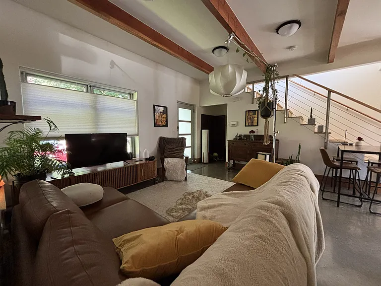 Living room with plenty of natural light, exposed beams, and polished concrete floors. Next to the entry door, a coat closet and shoe nook.