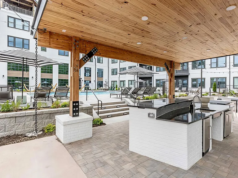 Full outdoor countertop with refrigerators under a modern pergola next to the pool