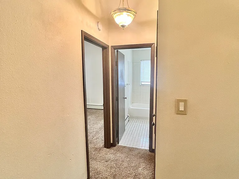 Inviting hallway with warm lighting leading to a cozy carpeted room and a pristine tiled bathroom.