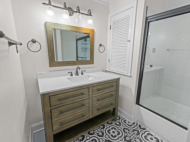 Stylish bathroom with wood-framed vanity, designer tile flooring, industrial lighting, and a glass-enclosed shower.