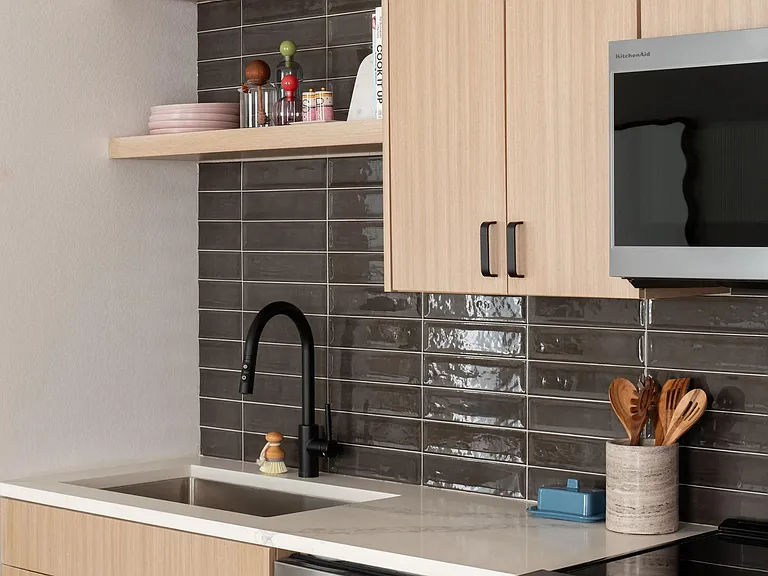 Streamlined cabinetry, open shelving, and a glossy tile backsplash bring warmth and texture to this thoughtfully designed kitchen.