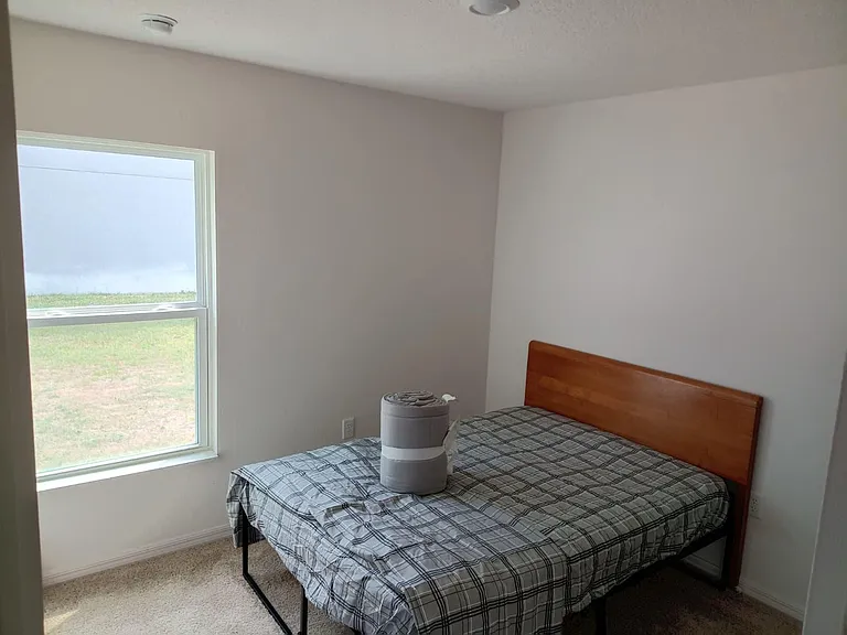 Private bedroom with a large window, neutral walls, and carpeted flooring, offering space for a full/queen bed setup.