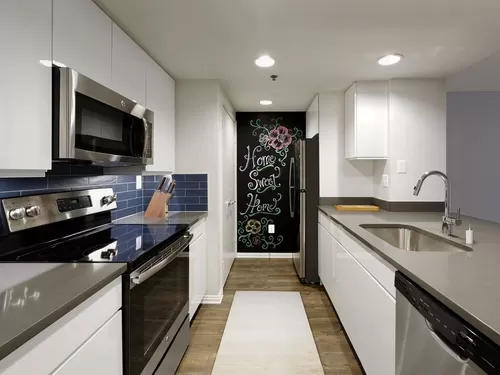 Newly Renovated Finish Package V kitchen with grey quartz countertops, blue tile backsplash, white cabinetry, stainless steel appliances, and hard surface plank flooring - AVA Ballston Square