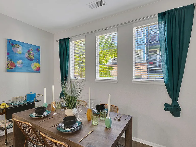 Inviting dining room featuring a modern table set with stylish dishware, vibrant artwork, and natural light filtering through chic green curtains.