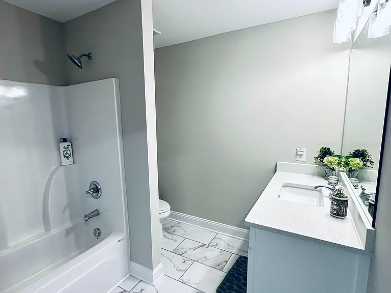 Updated full bath with tub/shower combo, spacious vanity, and large mirror, finished with marble-look tile flooring.