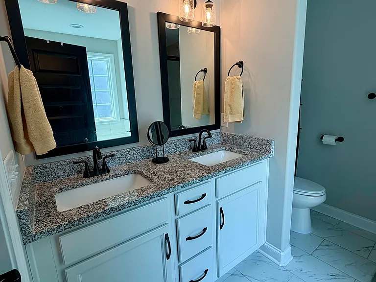 Updated bathroom with dual-sink vanity, granite countertop, and ample cabinet storage, plus tile flooring and modern lighting