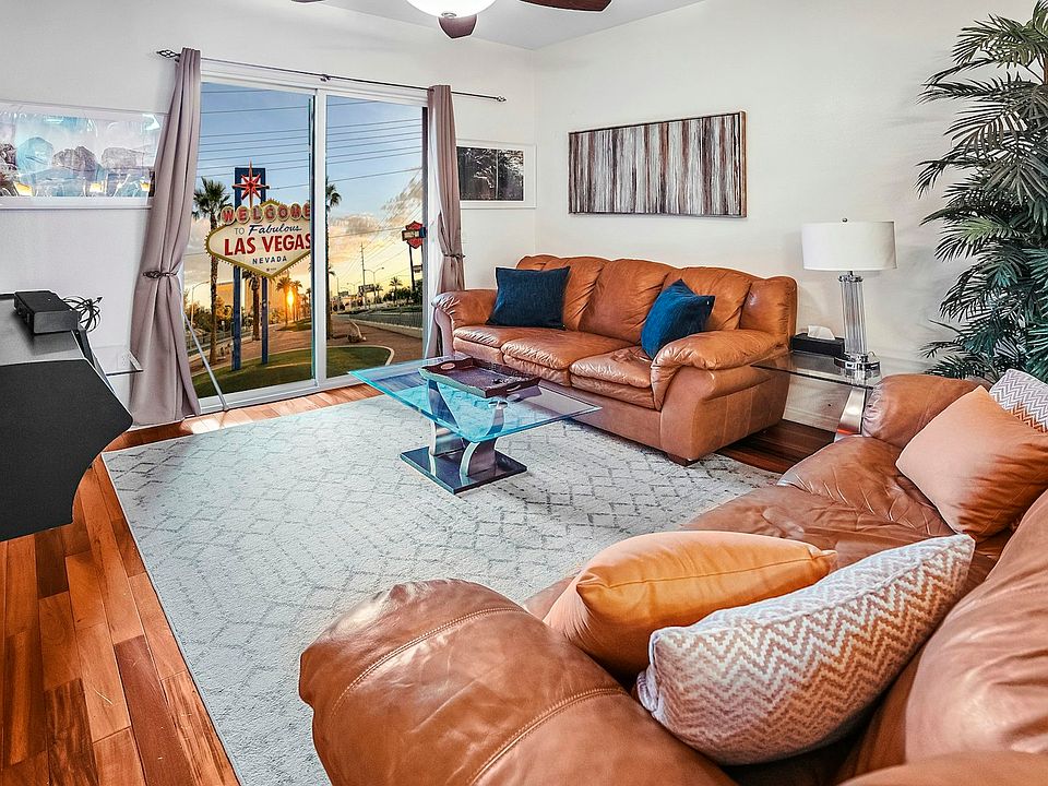 Fully furnished living room featuring two comfortable leather sofas, a coffee table with lamps, a stylish area rug, decorative artwork, and artificial plants for a warm and inviting atmosphere