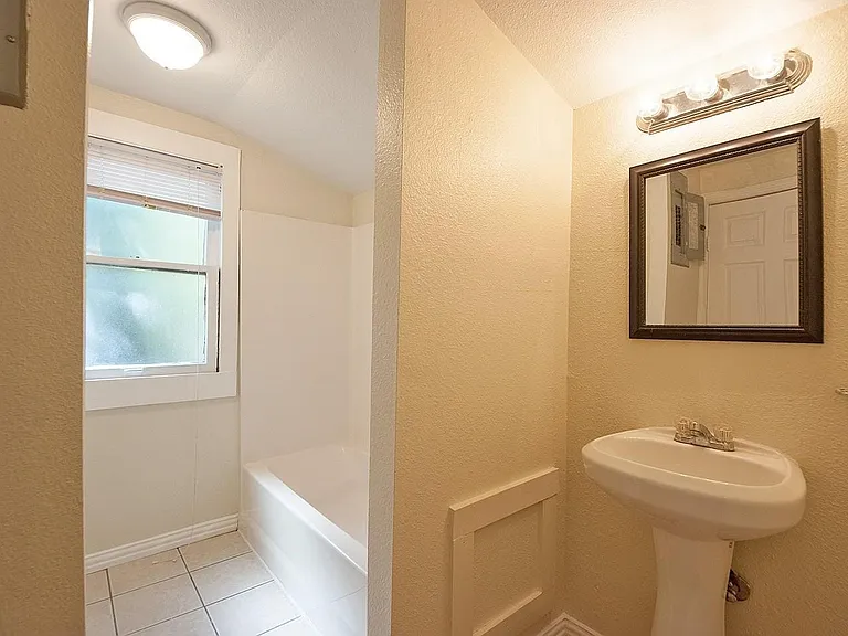 A bright bathroom with a sink, bathtub, and a window for ventilation and natural light.