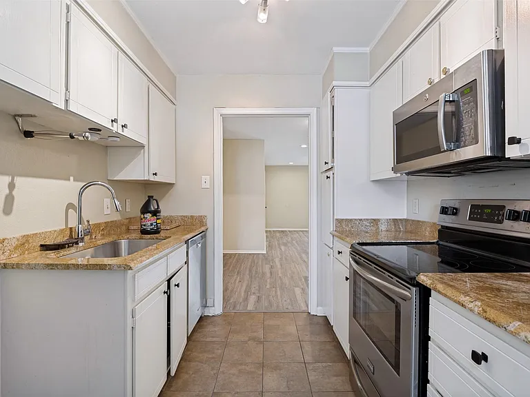 Galley kitchen featuring white cabinetry, stone-finish countertops, and stainless steel appliances including an oven range and built-in microwave