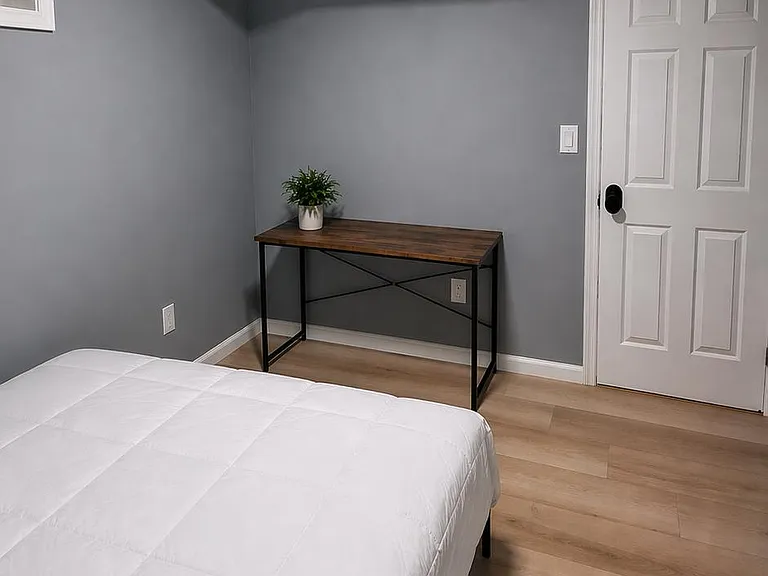 Private bedroom with wood-look flooring, neutral paint, and space for a desk or workspace setup.