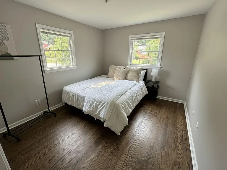Comfortable bedroom with hardwood floors, two windows for natural light, and space for a bed and nightstand.