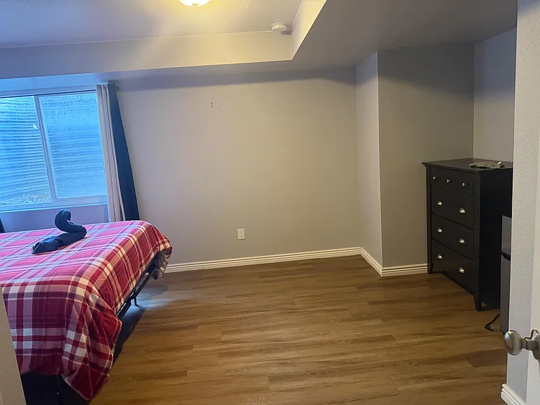 Bedroom with wood-style flooring, a large window with curtains, and space for a bed plus dresser or desk.
