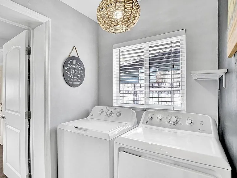 Dedicated laundry nook with full-size washer and dryer, overhead lighting, and a window with blinds for ventilation.
