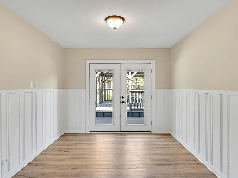 Dining room French doors lead to beautiful back yard with mature trees and covered deck. French doors have blinds inside the windows.