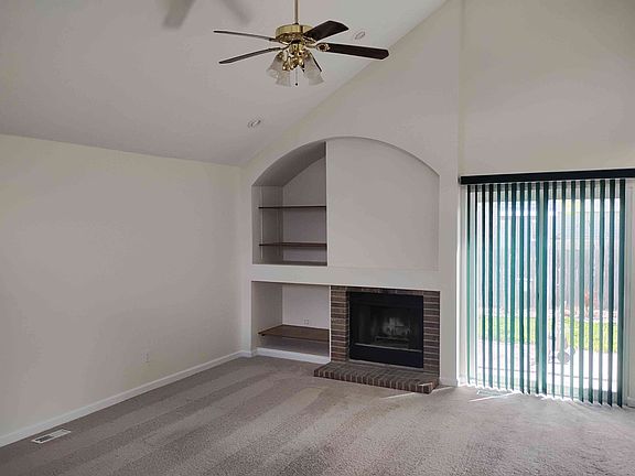 Living room has vaulted ceiling, bookshelves and a fireplace. Access to outdoor patio via a sliding door.
