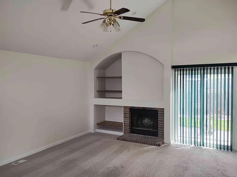 Living room has vaulted ceiling, bookshelves and a fireplace. Access to outdoor patio via a sliding door.