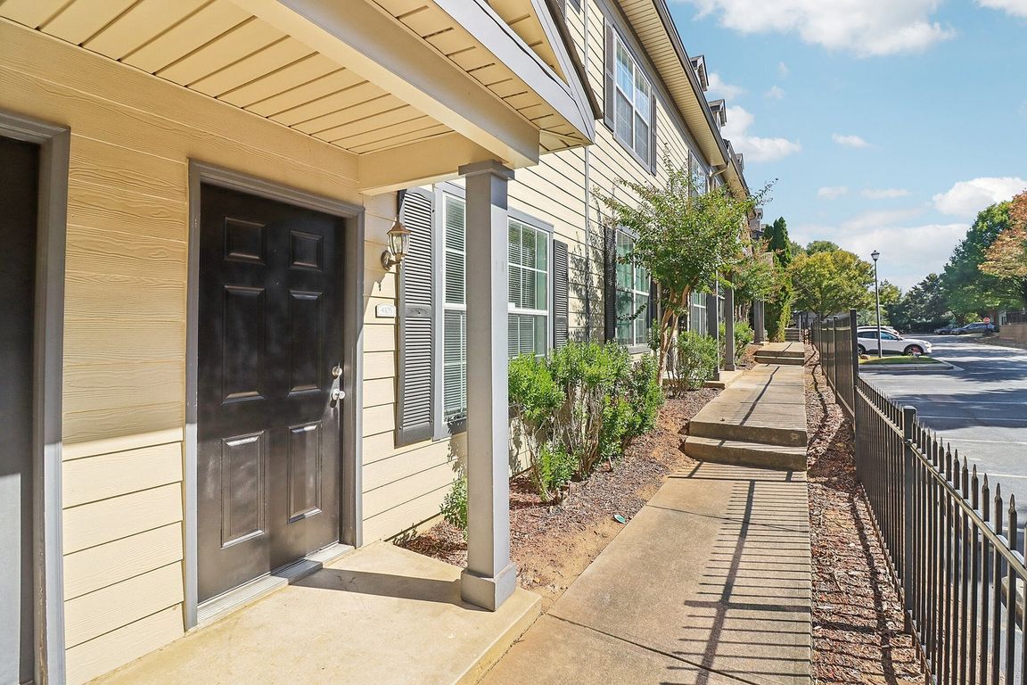 Charming apartment entrance with black door, surrounded by lush greenery and well-maintained pathway.
