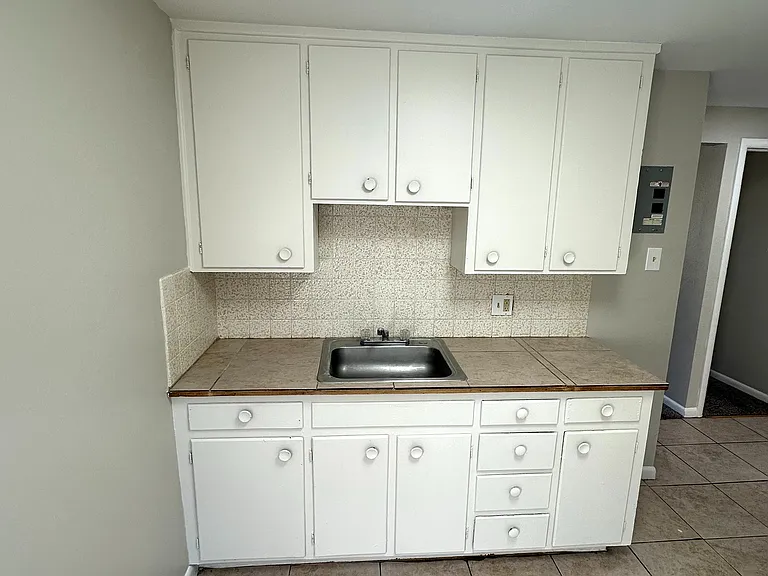 Bright kitchen featuring sleek white cabinetry, elegant tile flooring, and a stainless steel sink, perfect for modern living.