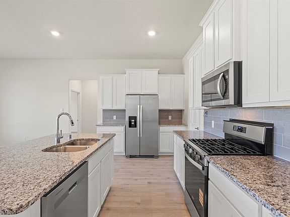 Kitchen featuring granite countertops, stainless steel appliances, white cabinetry, a double basin sink, and wood-finish flooring