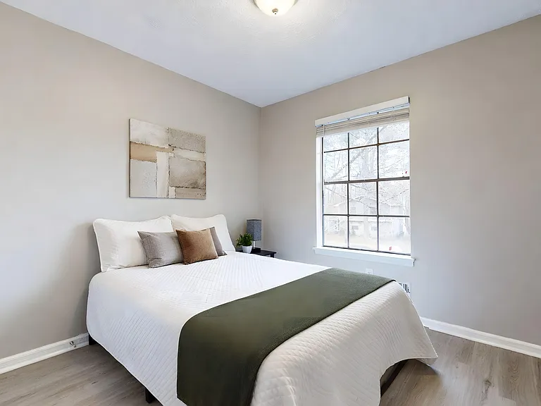 Furnished bedroom with a full bed, nightstand, and large window for natural light; neutral finishes and easy-care flooring.