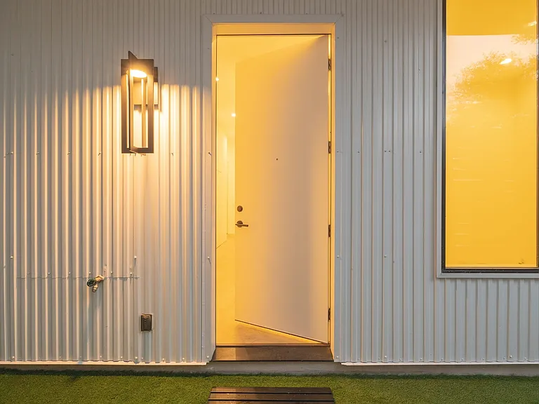 Entryway featuring a modern exterior wall sconce, corrugated metal siding, and a contrasting dark-framed window