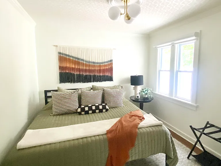 The first floor bedroom features a king bed and soft bedding, a wall mirror, a closet with hangers, and a luggage rack. A large window offers a lovely view of the back patio, and a full bathroom with a tiled walk-in shower is just steps away.