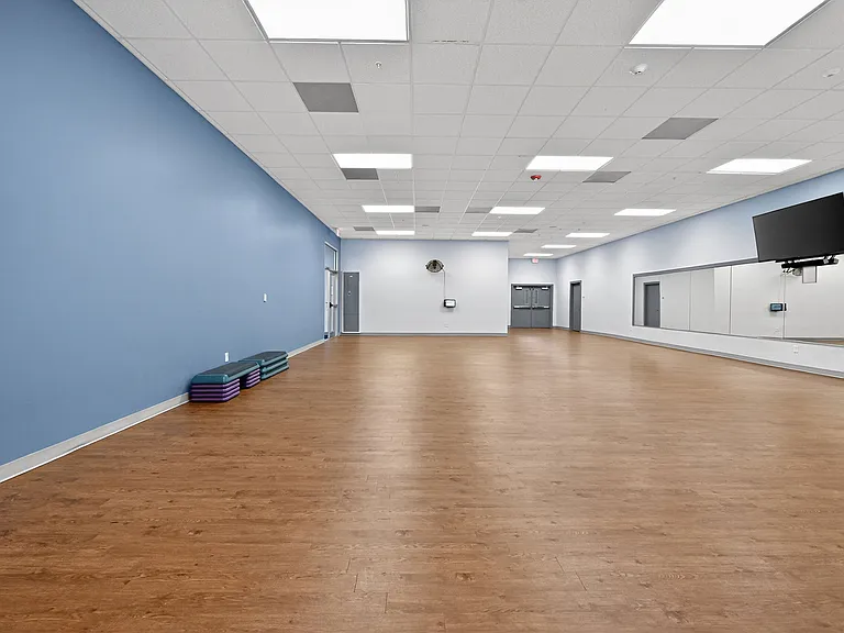 Spacious fitness studio with polished hardwood floors, mirrored wall, and vibrant blue accent wall, perfect for yoga or aerobics classes.