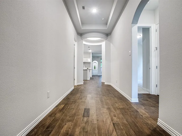 Hallway featuring wood-finish flooring, white baseboards, a tray ceiling with recessed lighting, and arched doorways