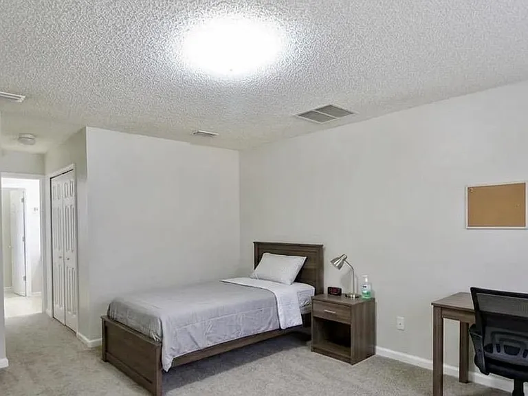 Spacious carpeted bedroom with a full bed, nightstand and lamp, plus a dedicated desk area and closet storage.