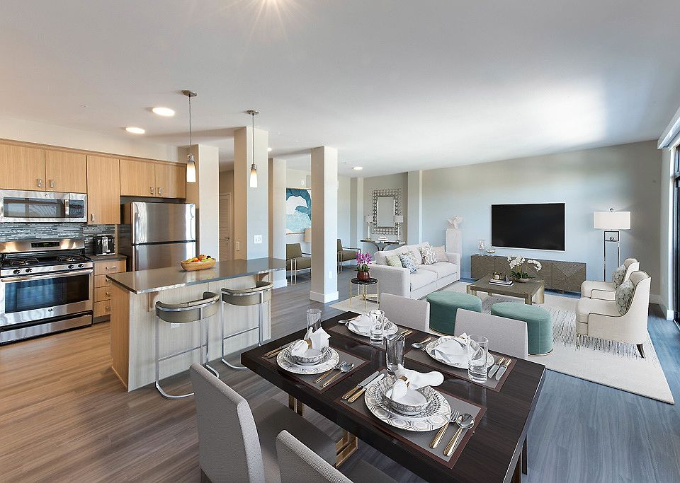 Staged open concept kitchen with island with stainless steel appliances and living room with hardwood style flooring.