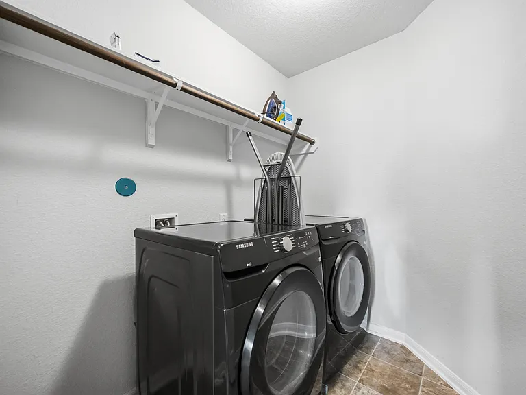 Dedicated laundry closet with side-by-side washer and dryer plus a shelf and hanging rod for convenient storage.