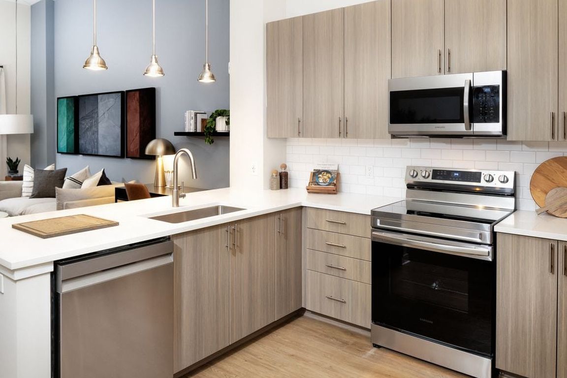Modern kitchen with oak cabinetry, white tile backsplash, white quartz countertops, stainless steel appliances, and pendant lighting