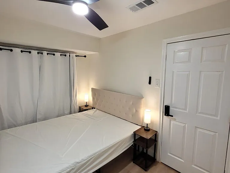 Furnished bedroom with ceiling fan, bedside tables and lamps, and a window with curtains for privacy and light control.