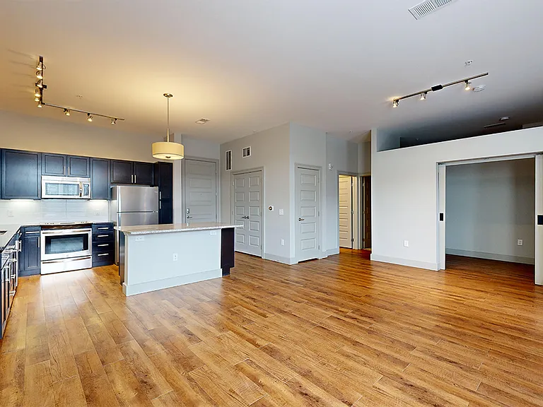 Apartment kitchen with stainless steel appliances, dining and living room with wood-style flooring.