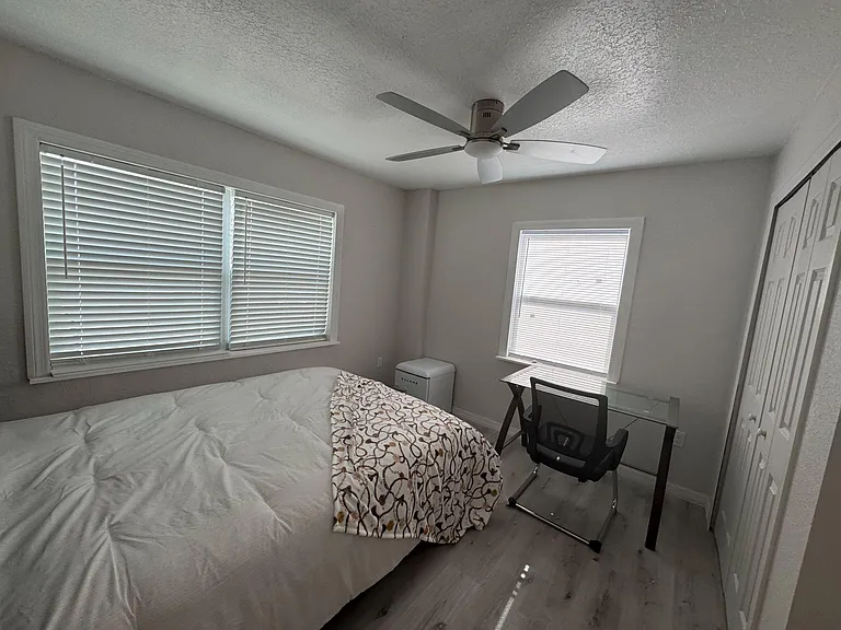 Private bedroom with two windows, ceiling fan, and a dedicated desk area with chair, plus closet storage.