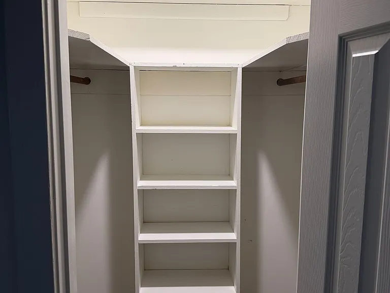 Walk-in closet with built-in center shelving and dual hanging rods for organized clothing and linen storage.