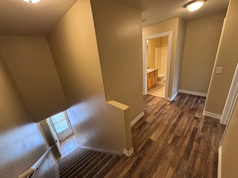 Top of stairs looking towards guest full bathroom. New LVP flooring throughout hallway and bedrooms.