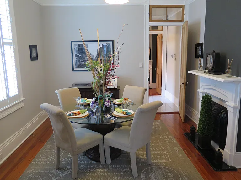 The dining room decor consists of a topiary, stylish French letter rug, 54" glass table and parsons chairs.