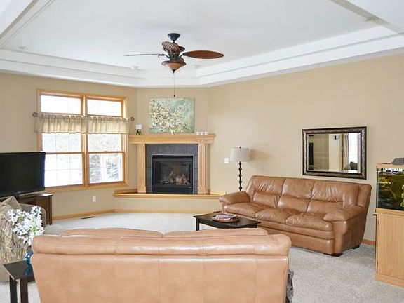 The view is of the main living room from the front entry. Large windows provide natural light and a wonderful view of the wooded backyard and stunning sunsets!  The room features a corner fireplace which adds warmth on cold evenings.  Neutral colors and the unique ceiling lines enhance the beauty of this space which opens into the kitchen and dining areas.