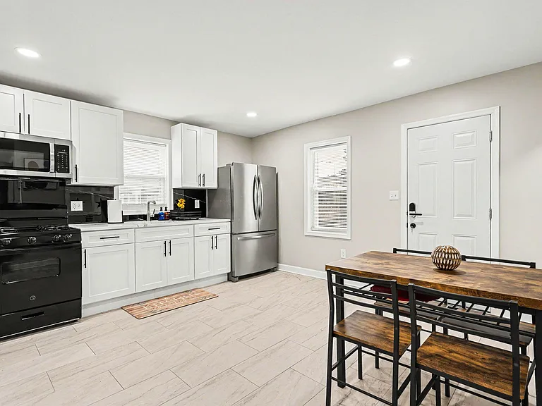 Eat-in kitchen with white cabinetry, stainless fridge, gas range, and a dining table set beside two windows.
