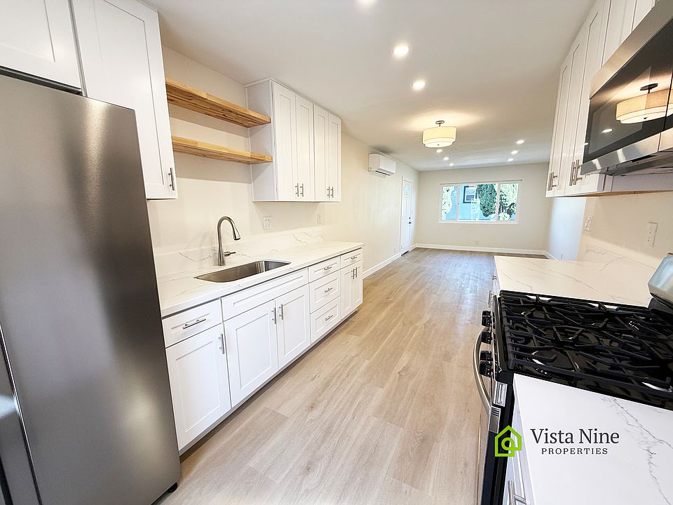 Beautiful kitchen with plenty of storage with white cabinets, wood accent shelves, stainless steel appliances and sink, veined quartz countertops