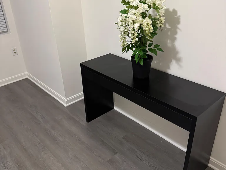 Open flex area with wood-look flooring and a sleek console table, ideal for a drop zone or small workspace.