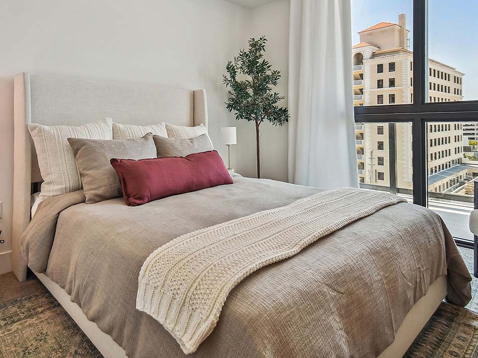Griffis West Palm apartment bedroom with pattern rug, plush bed with headboard, and large window.
