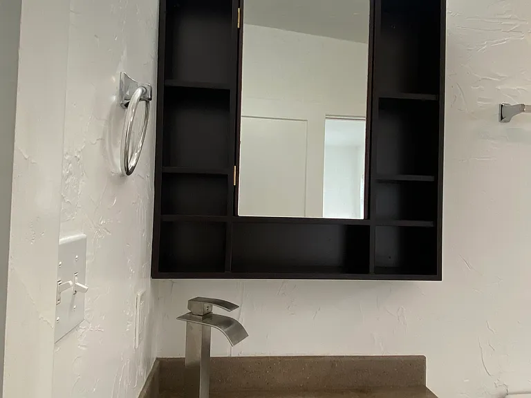Bright, well-lit vanity with a recessed medicine cabinet behind the mirror and complementary shelving on either side for pratical or decorative use.