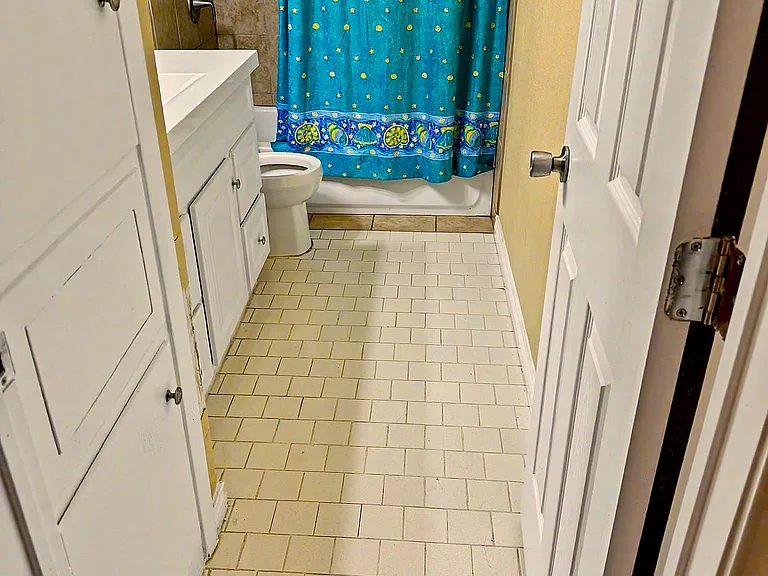 Full bathroom with a tub/shower combo, tiled surround, vanity storage, and a window for ventilation and natural light.
