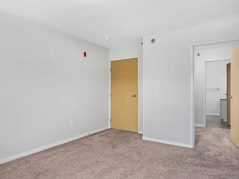 Bright empty room with clean beige carpet, white walls, and two doors leading to additional spaces. Bright empty room with clean beige carpet, white walls, and two doors leading to additional spaces.