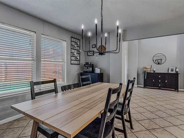 Dining area featuring a modern black chandelier, two windows with blinds, and tiled flooring